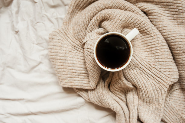 黑咖啡在白色的杯子在针织米色毛衣皱褶的床上，俯视图，单色舒适的早餐图片图片下载