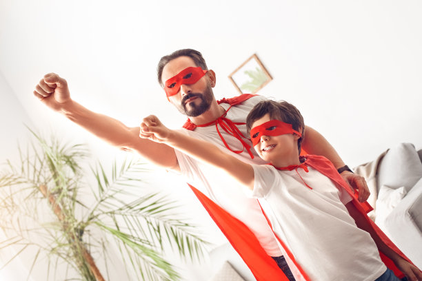 爸爸和儿子穿着超级英雄的服装站在家里，双手高高飞起来兴奋不已图片下载