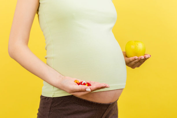 近距离的孕妇选择一个苹果和一堆药丸在彩色背景与复制空间。怀孕期间服用维生素图片下载