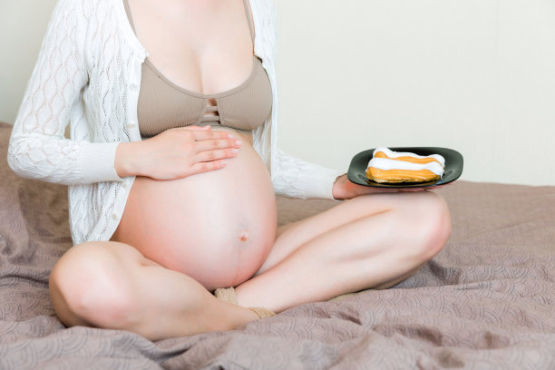 近距离的饥饿孕妇是吃糕点与极大的乐趣放松在床上在家里。快乐怀孕概念图片下载