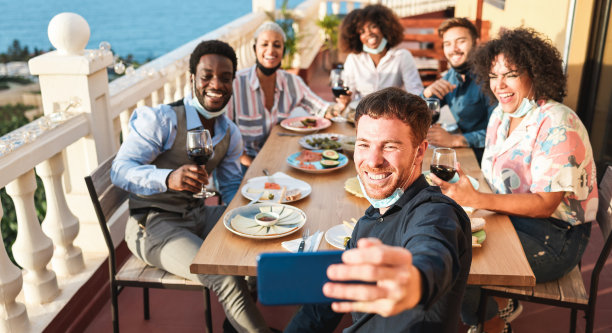 年轻的多种族的人自拍，而戴着防护面具-快乐的朋友正在做晚餐在家里的院子室外-社会距离概念-关注男人红头发脸图片下载