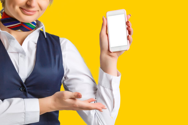 美丽的年轻空姐拿着智能手机孤立在黄色，橙色，背景图片下载