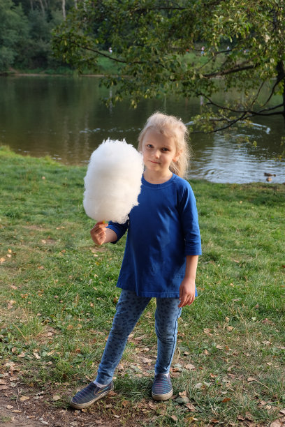 一个小女孩在公园的树下吃棉花糖。图片下载