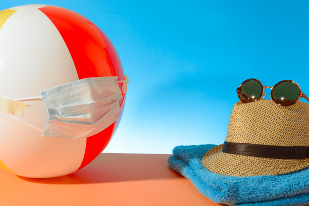 带医用面具的沙滩彩球。草帽。太阳镜。毛巾。2019冠状病毒病流行期间的暑假检疫概念照片。图片下载