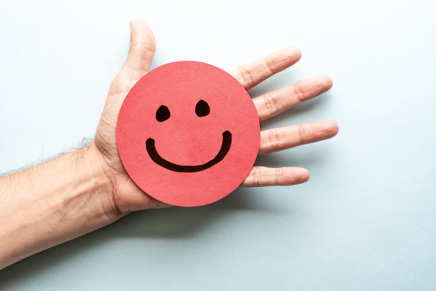 在红纸上画一个快乐的微笑表情，手和蓝色的背景图片下载