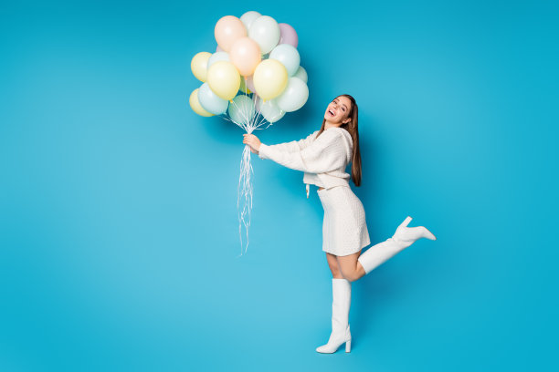 完整尺寸的照片迷人的内容，偷拍的女孩尝试抓住许多气球，她在周年庆典穿好看的衣服，鞋子孤立的蓝色背景图片下载