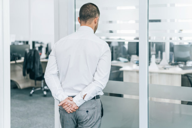 在COVID-19期间，忧心忡忡的商人双手背后，看着空荡荡的办公室图片下载