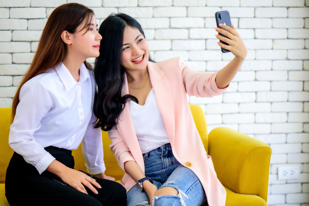 美丽年轻幸福的亚洲女人微笑着一起用手机或智能手机自拍早上在客厅。幸福友谊关系概念。图片下载