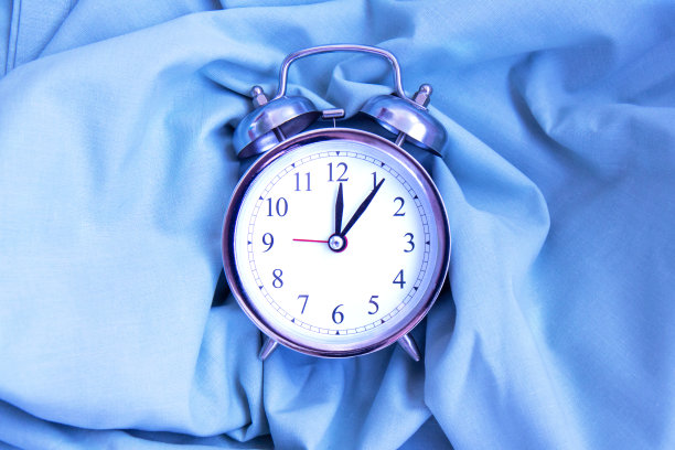 美丽的银色古董闹钟上的褶皱蓝色自然织物的背景与阴影图片下载