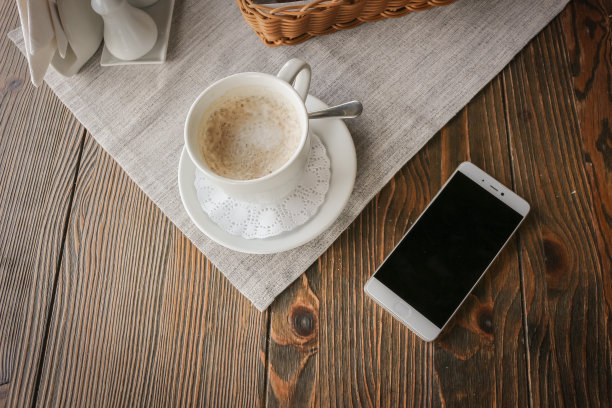 俯视图智能手机和一杯咖啡在一个质朴的木桌上。图片下载