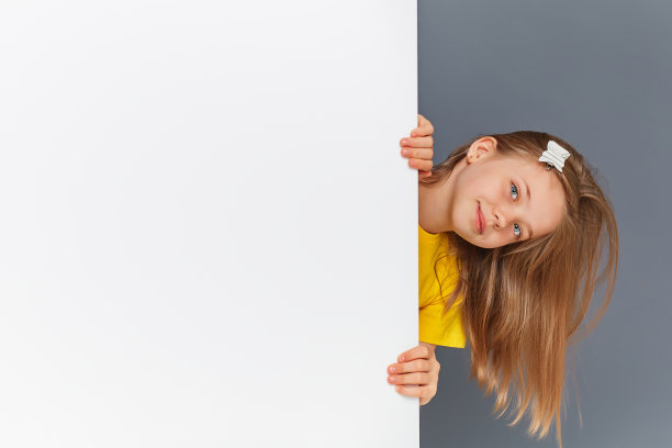 一个穿着黄色衣服的有趣的十几岁的女孩看着白色的墙标志。图片下载