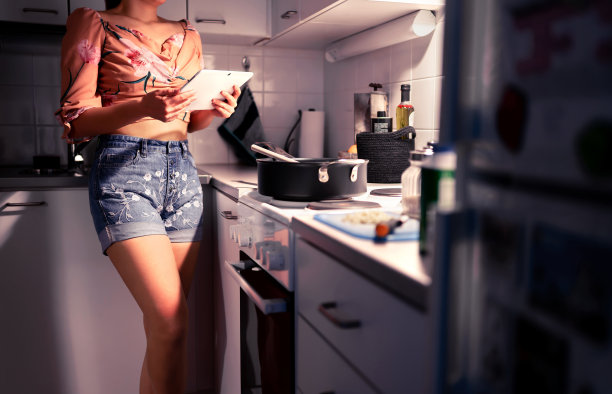 妇女做饭和使用平板电脑在家庭厨房。网上的晚餐食谱。互联网厨师类。学生阅读一个网站并学习做一份健康的素食餐。图片下载