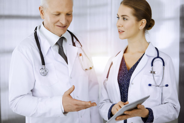 老年自信的医生和女医生讨论当前的疾病治疗，而站在阳光诊所。团队合作在医学图片下载