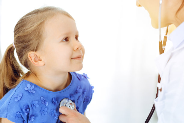 医生在阳光诊所用听诊器检查儿童。病人穿着蓝色连衣裙，开心微笑的女孩正在进行常规的医学检查图片下载