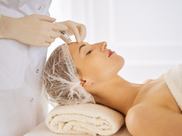 闭着眼睛接受美容注射的美女。美容师医生用注射器给女性脸部做美容手术图片下载