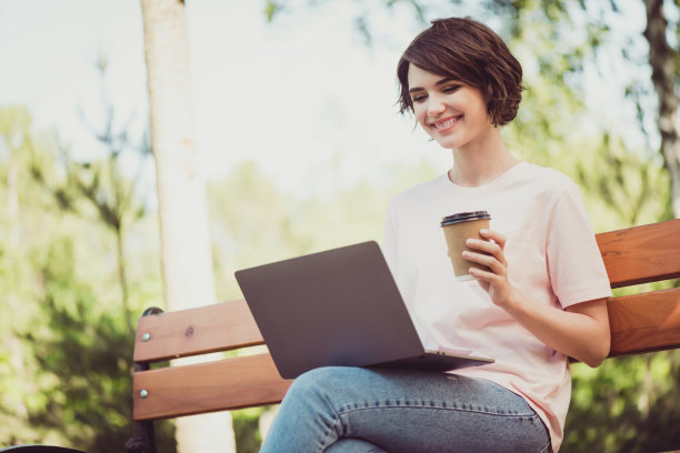 迷人的可爱的女士的照片愉快的看坐在长椅喝咖啡手提电脑喜气开朗的微笑打字浏览新闻分享帖子朋友在网上穿白衬衫在户外图片下载