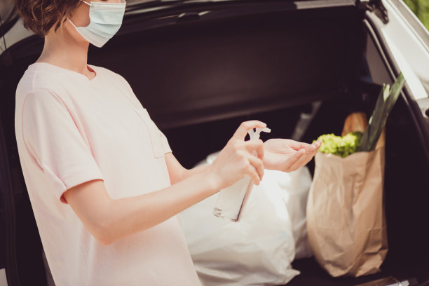 照片中的女孩医疗口罩，驾驶汽车，购买超市购物袋，在冠状病毒感染的检疫，安全生活，洗手，喷雾，手，消毒剂，在镇中心外图片下载