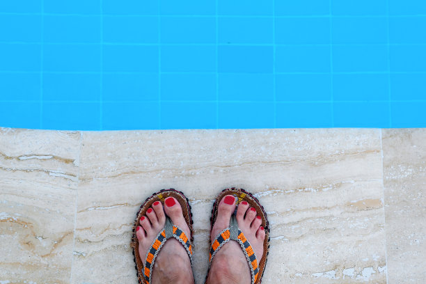 穿着拖鞋的女人的脚在泳池边。图片下载