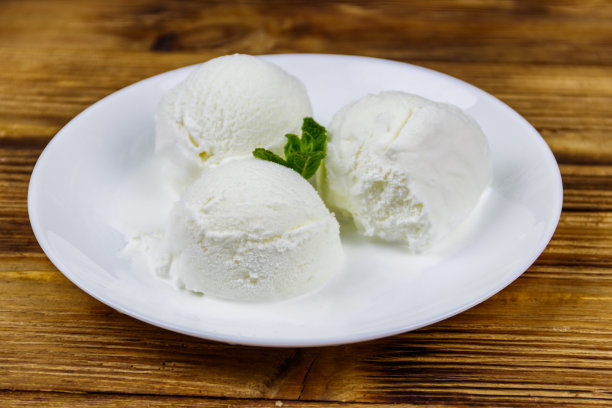 香草冰淇淋装在白色的盘子里，放在一张木桌上图片下载
