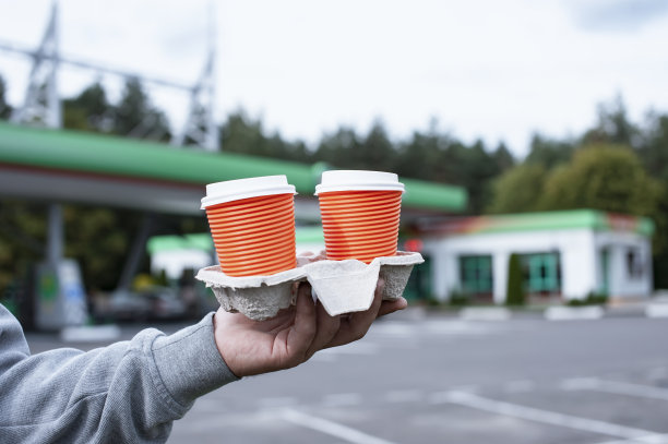 一个男人在加油站手里拿着两杯咖啡。图片下载