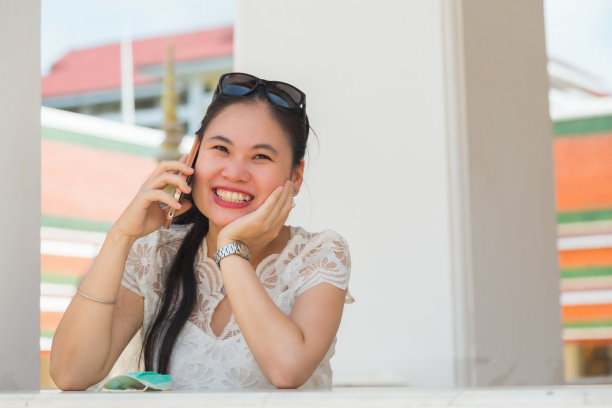 近距离观察一名年轻的亚洲女子，她穿着一件白色衬衫，用手托着下巴，在寺庙里戴着面具与手机交谈图片下载