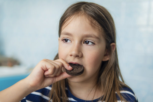 一个女孩坐在家里的厨房里吃一块圆形的巧克力饼干的特写镜头。有害但美味的食物。甜味。图片下载