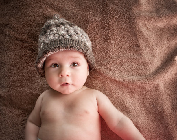 快乐的婴儿在温暖的帽子躺在一个蓬松的棕色毯子上图片下载