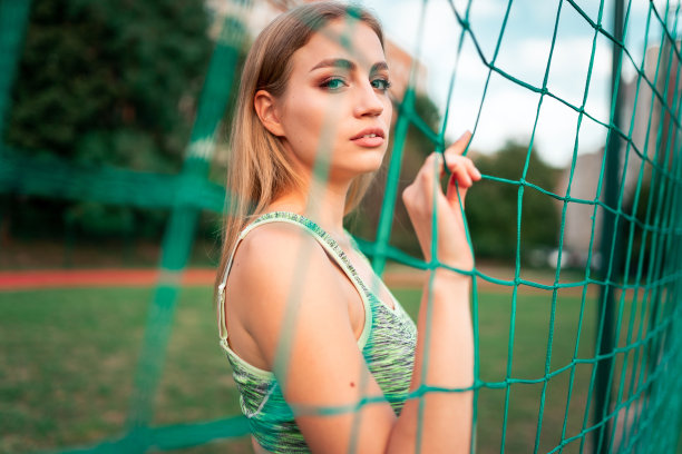 一个美丽的体育女孩的肖像与美丽的眼睛谁站在球门后的网图片下载