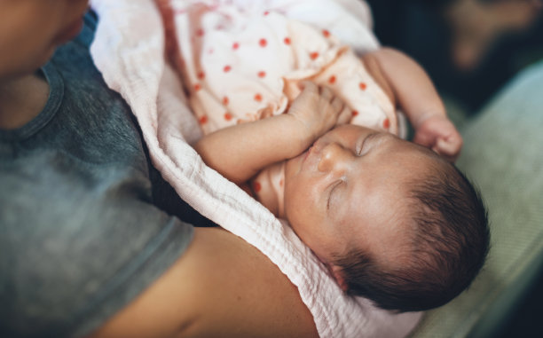 上面的照片，一个白人婴儿在她妈妈的手里睡觉和做梦，穿着粉红色可爱的裙子图片下载