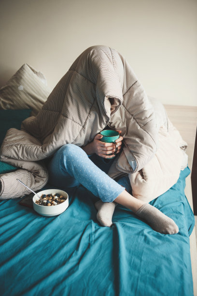 白种人妇女在床上盖着被子喝着茶，吃着麦片，穿着蓝色的睡衣图片下载