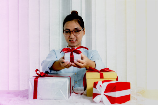身穿蓝色衬衫的女子拿着一个用红色丝带系着的白色礼盒，礼物是为圣诞节、情人节等特殊节日准备的图片下载