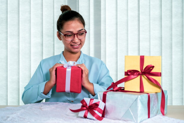 一个穿着蓝色衬衫的女人拿着一个红色的礼品盒，上面系着红色的丝带，这是为圣诞节、情人节等特殊节日准备的礼物图片下载