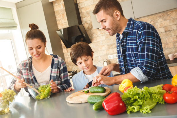 一家人一起站在厨房里，儿子听着父亲切黄瓜讲解如何做沙拉，母亲开心地搅拌配料图片下载