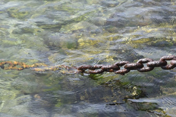 系泊船用的生锈的锚链，系在岸边的岩石上图片下载
