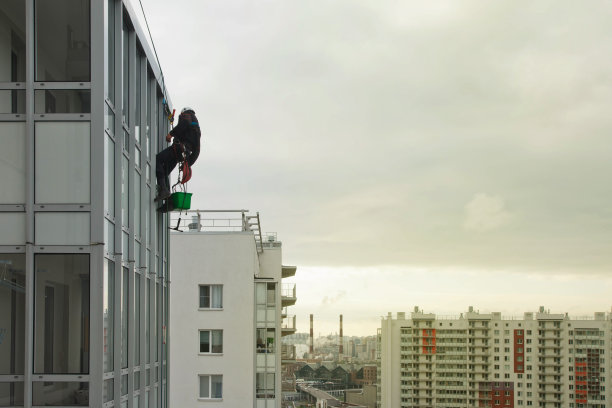 工业登山工人在清洗外立面玻璃时，悬停在住宅楼上方图片下载