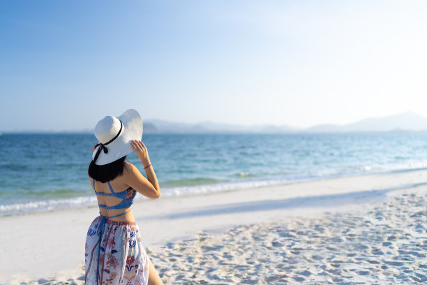 快乐的女人戴着海滩太阳帽在海滩上图片下载