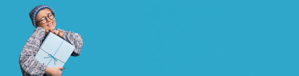 一个戴着帽子和眼镜的金发女人在一个有自由空间的蓝色墙上大力宣传一些东西的时候拥抱着一份礼物图片下载