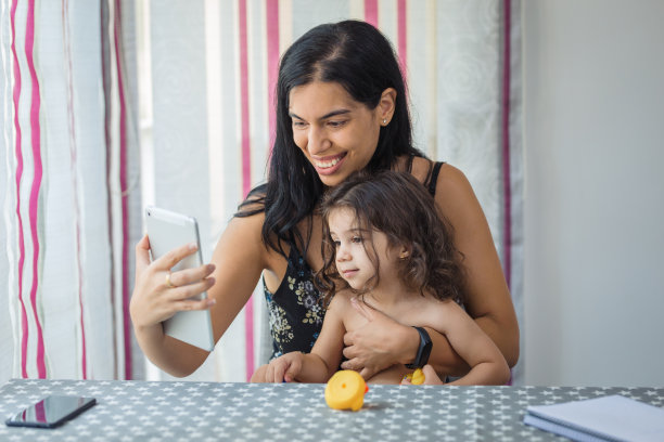 母亲和女儿在家里的餐厅里使用平板电脑。图片下载