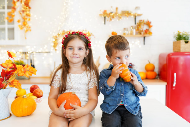 可爱的小朋友们正坐在秋天厨房的桌子上雕刻南瓜。快乐的一家人在为万圣节做准备。家里有有趣的孩子。图片下载