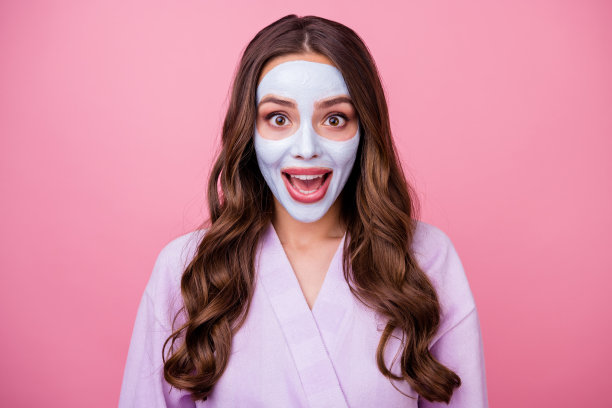照片肖像的年轻快乐惊讶的女人微笑印象深刻的剥落面膜穿着浴袍隔离在粉红色的背景图片下载