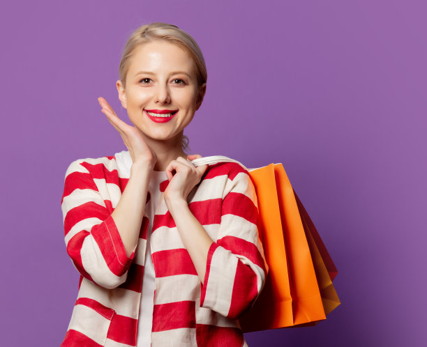 漂亮的金发在红色夹克与购物袋在紫色的背景图片下载
