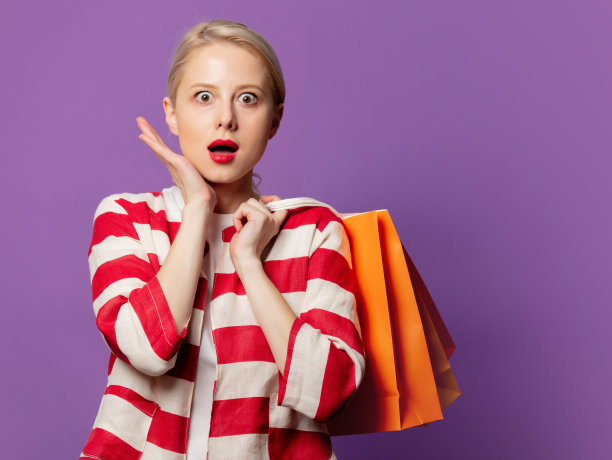 漂亮的金发在红色夹克与购物袋在紫色的背景图片下载