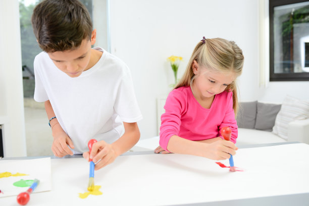两个漂亮的小男孩和女孩用彩色颜料在白纸上手绘图片下载