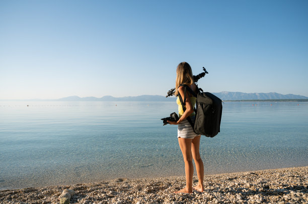 年轻的女摄影师站在美丽的卵石滩上。图片下载