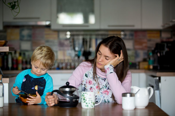 疲惫的母亲，妇女在早上喝咖啡，而孩子吃早餐图片下载