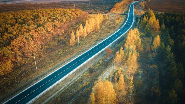 鸟瞰图的道路在美丽的橙色森林在秋天日落。五彩缤纷的风景与道路，树木在秋天。俯视图从嗡嗡的蜿蜒道路。图片下载