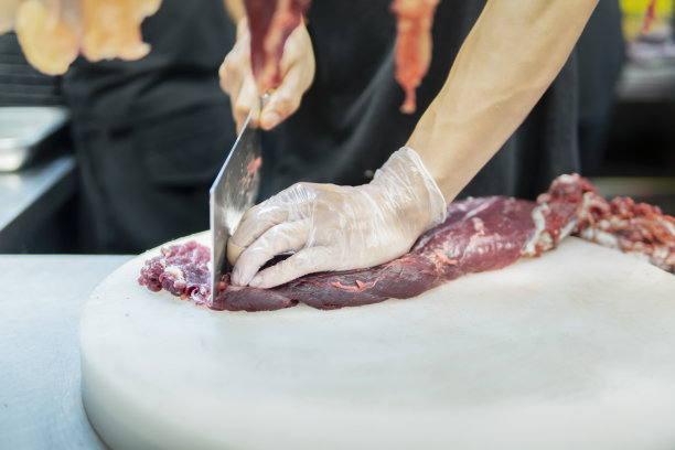 在一家牛肉火锅餐厅的开放式厨房里，厨师在挂着的切碎的生肉后面用刀切牛肉图片下载