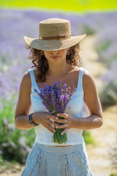 戴着草帽的女人在薰衣草田里捧着薰衣草花。图片下载