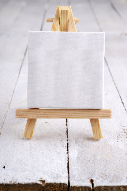 木桌上的一个小画架，上面铺着白布。微型画配件。光背景。图片下载