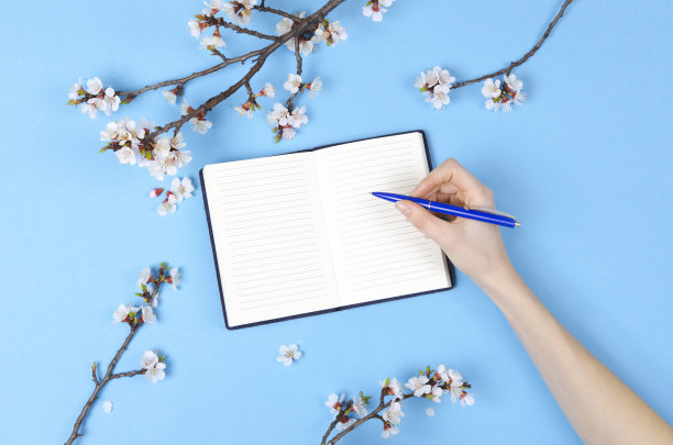 女孩正在写未来计划的愿望清单。用鲜花、记事本平铺构图图片下载